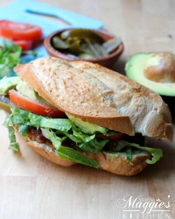 Torta de Milanesa (Mexican Fried Chicken Sandwich) on a wooden surface surrounded by its ingredients.