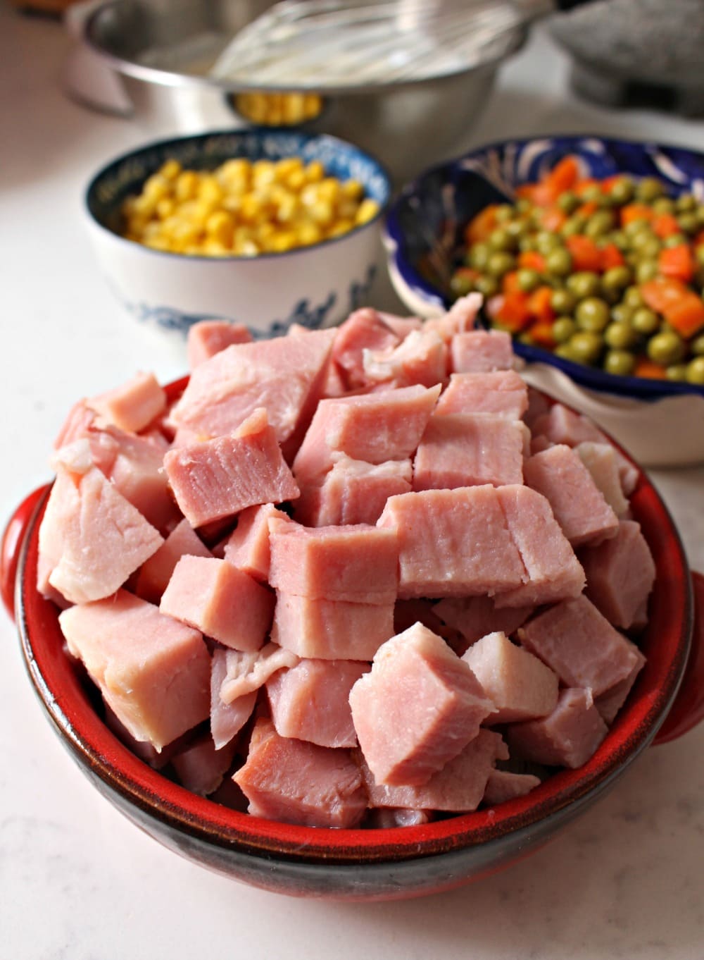 Cubed ham in a red bowl next to the other ingredients for Mexican pasta salad.