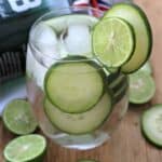 Cucumber Gin Cocktail served in a clear glass and surrounded by cucumber and lime slices.