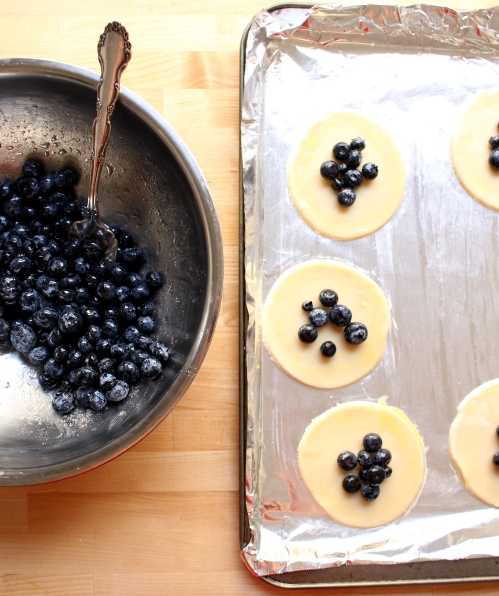 A sheet pan with pie dough and a bowl of blueberry filling next to it. 