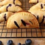 Blueberry Empanadas (or Blueberry Handpies) on a cooling rack surrounded by fresh blueberries.