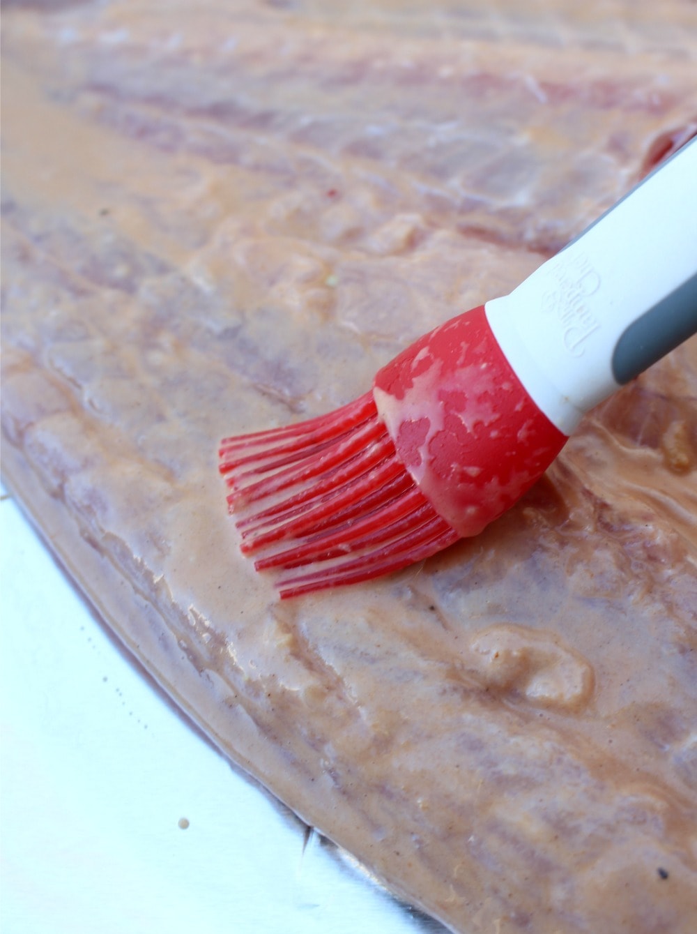 A red brush brushing the marinating sauce on a fish.