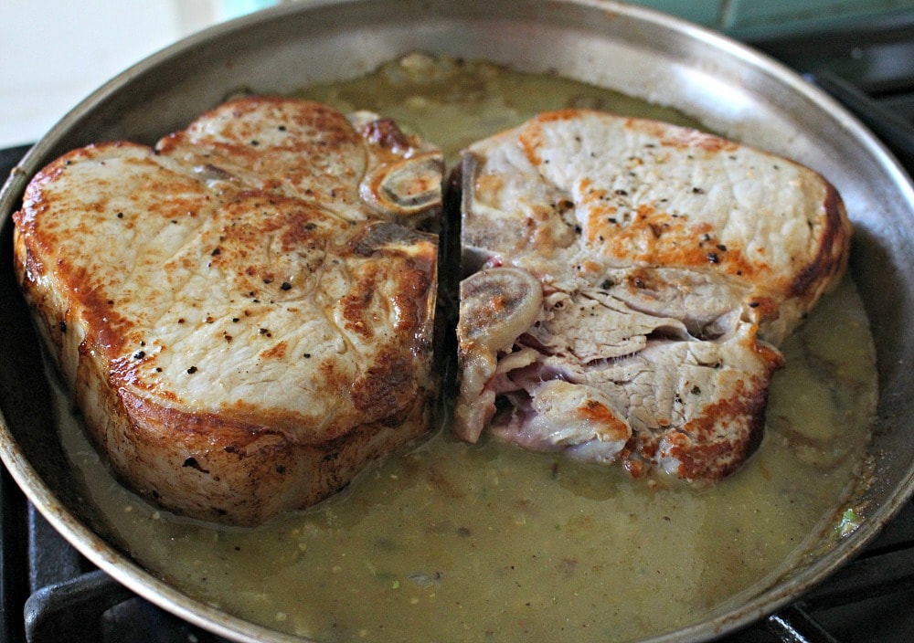 Pork chops cooking in a skillet with salsa verde.