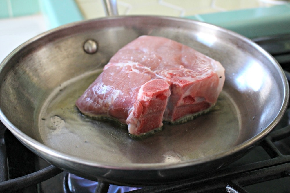 A pork chop searing in a skillet. 