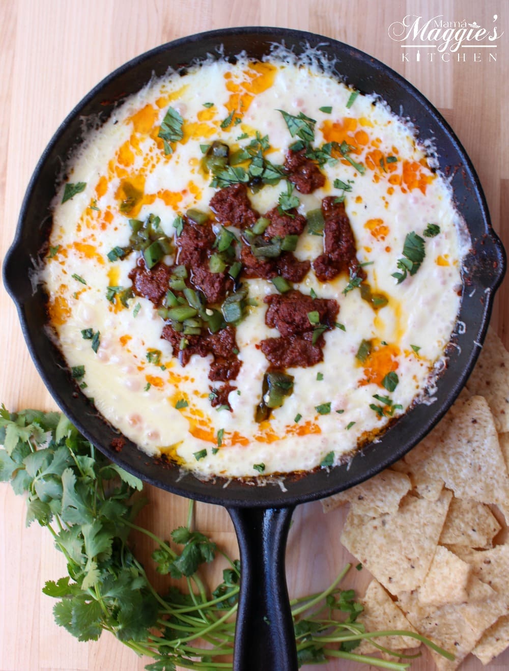 Queso Fundido Con Chorizo in a black iron skillet surrounded by corn chips and cilantro. 