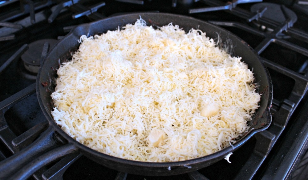 A mountain of shredded white cheese in a black iron skillet.