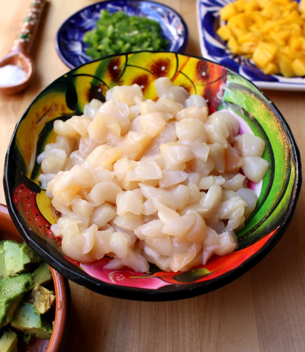 Chopped scallops in a decorative bowl surrounded by other ingredients for Scallop Ceviche.