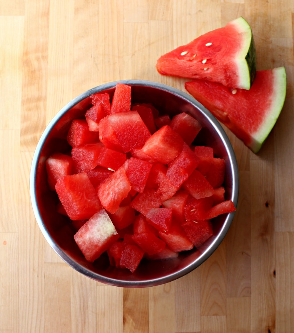 Diced watermelon in a bowl next to two watermelon slices.