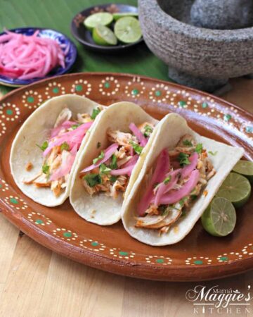 Pollo Pibili tacos on a decorative clay plate topped with red pickled onions.