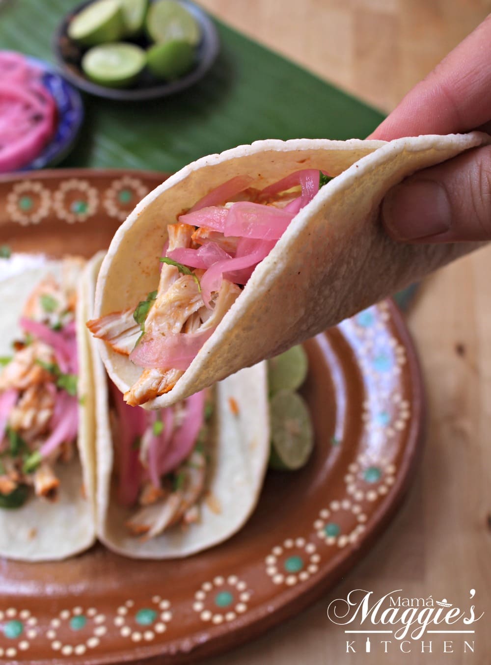 Hand holding a Pollo Pibil Taco topped with Mexican pickled onions. 