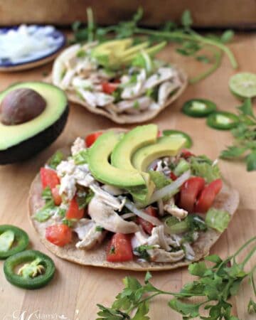 A tostada of Salpicon de Pollo topped with avocado slices surrounded by cilantro and jalapeno.