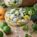 Scallop ceviche in a champagne glass surrounded by cilantro and lime.