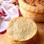 A stack of corn tortillas next to a tortilla holder and decorative kitchen towel.
