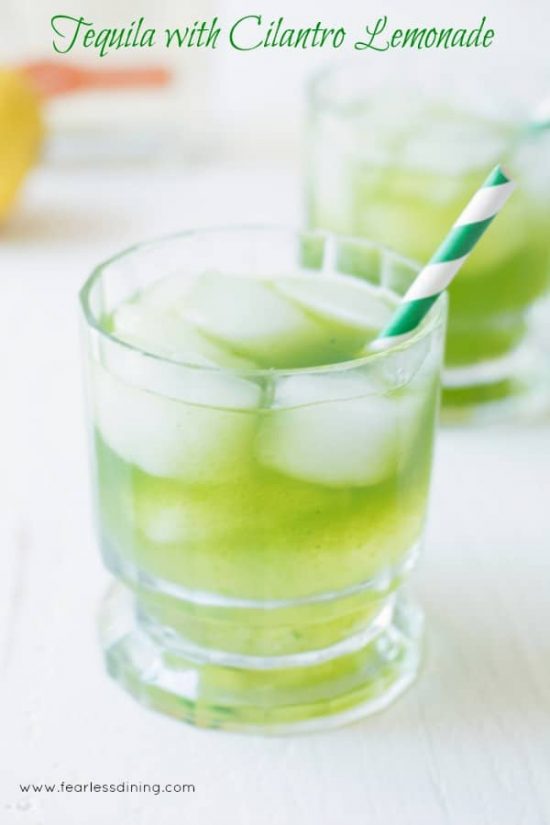 Tequila lemonade with cilantro served in a glass with ice and a green striped straw.