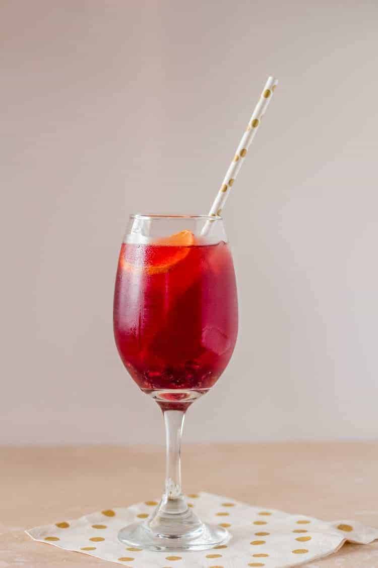 A Tequila Cocktail with Blood Orange and Pomegranate served in a wine glass and a striped straw.