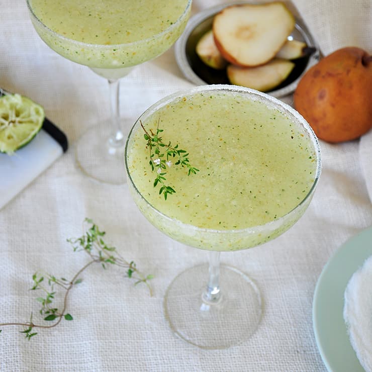 Frozen Thyme and Pear Margarita topped with a sprig of thyme on a white tablecloth.