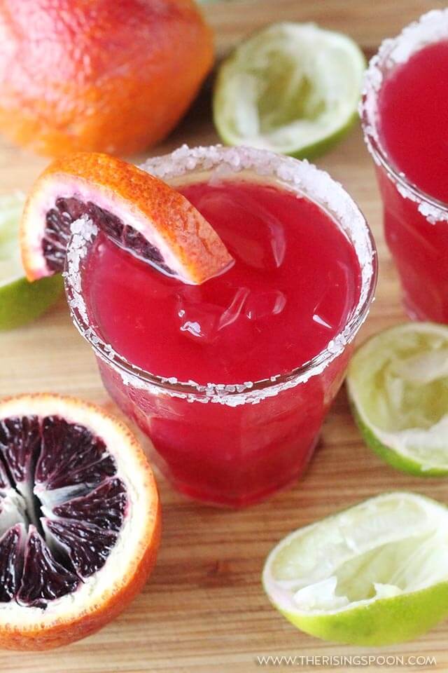 A Blood Orange Margarita served in a salt rimmed glass and topped with a wedge of blood orange.