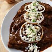 Enchiladas Dulces (Sweet Enchiladas) on a white plate topped with queso fresco and onion slices.