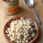 Hominy on a clay plate next to a hominy can and silver spoon.