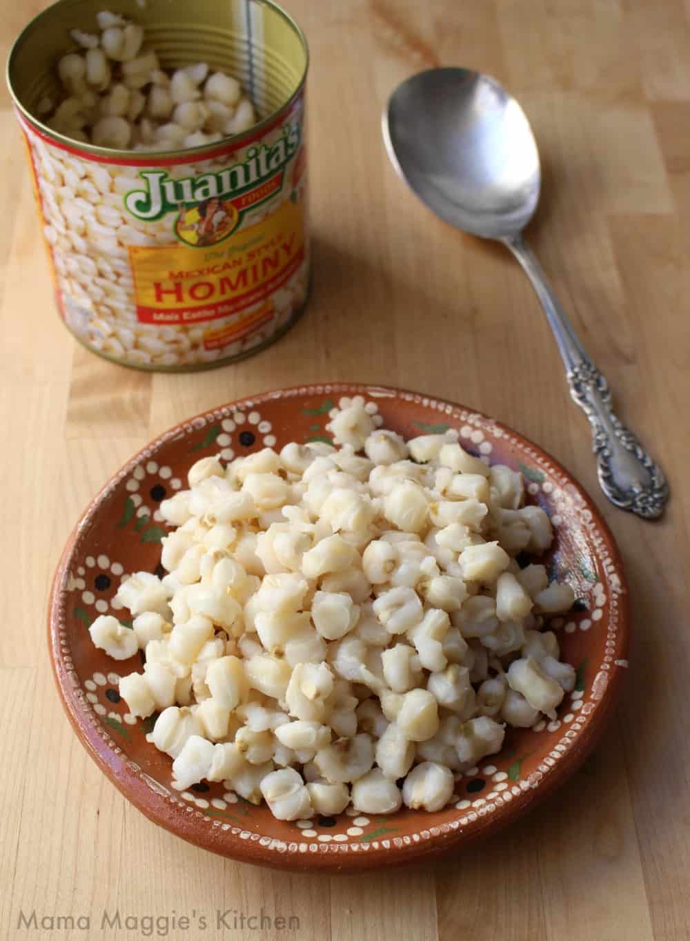 Hominy on a clay plate next to a hominy can and silver spoon.