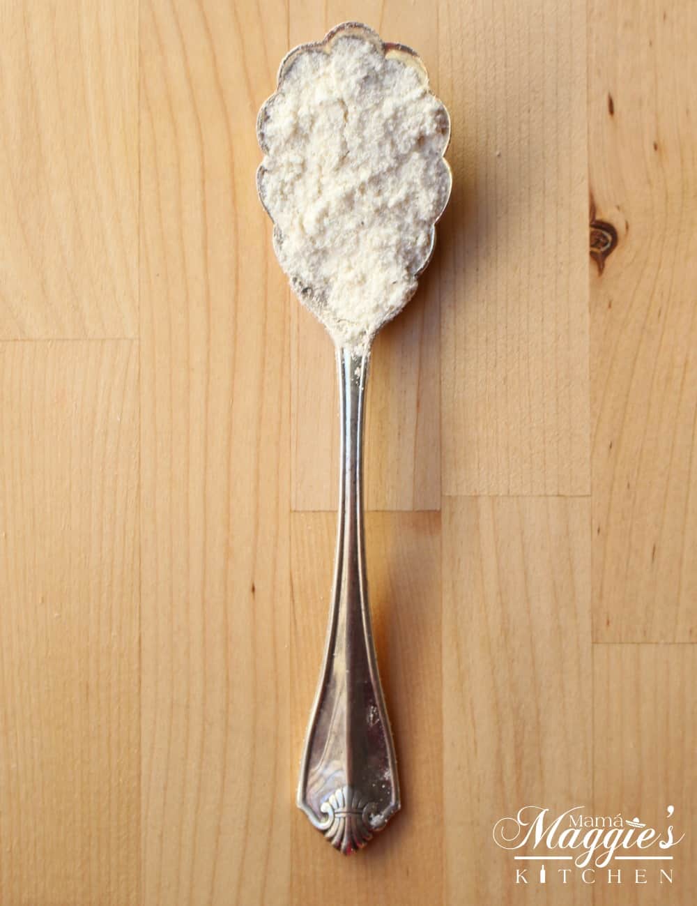 A spoon holding masa harina on a wooden surface.