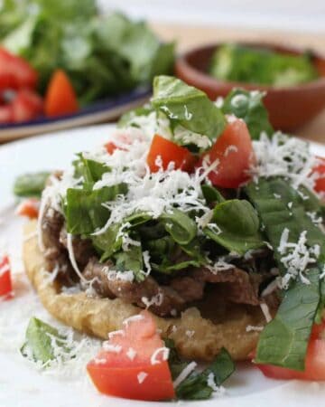 A sope topped with carne asada, lettuce, tomatoes, and cotija cheese.