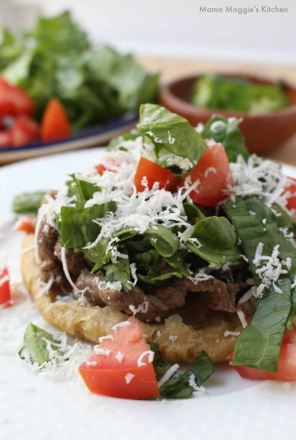 A sope topped with carne asada, lettuce, tomatoes, and cotija cheese.