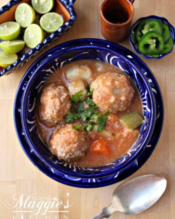 Albondigas en Caldillo (or Mexican Meatball Soup) in a decorative blue bowl next to lime and a spoon.