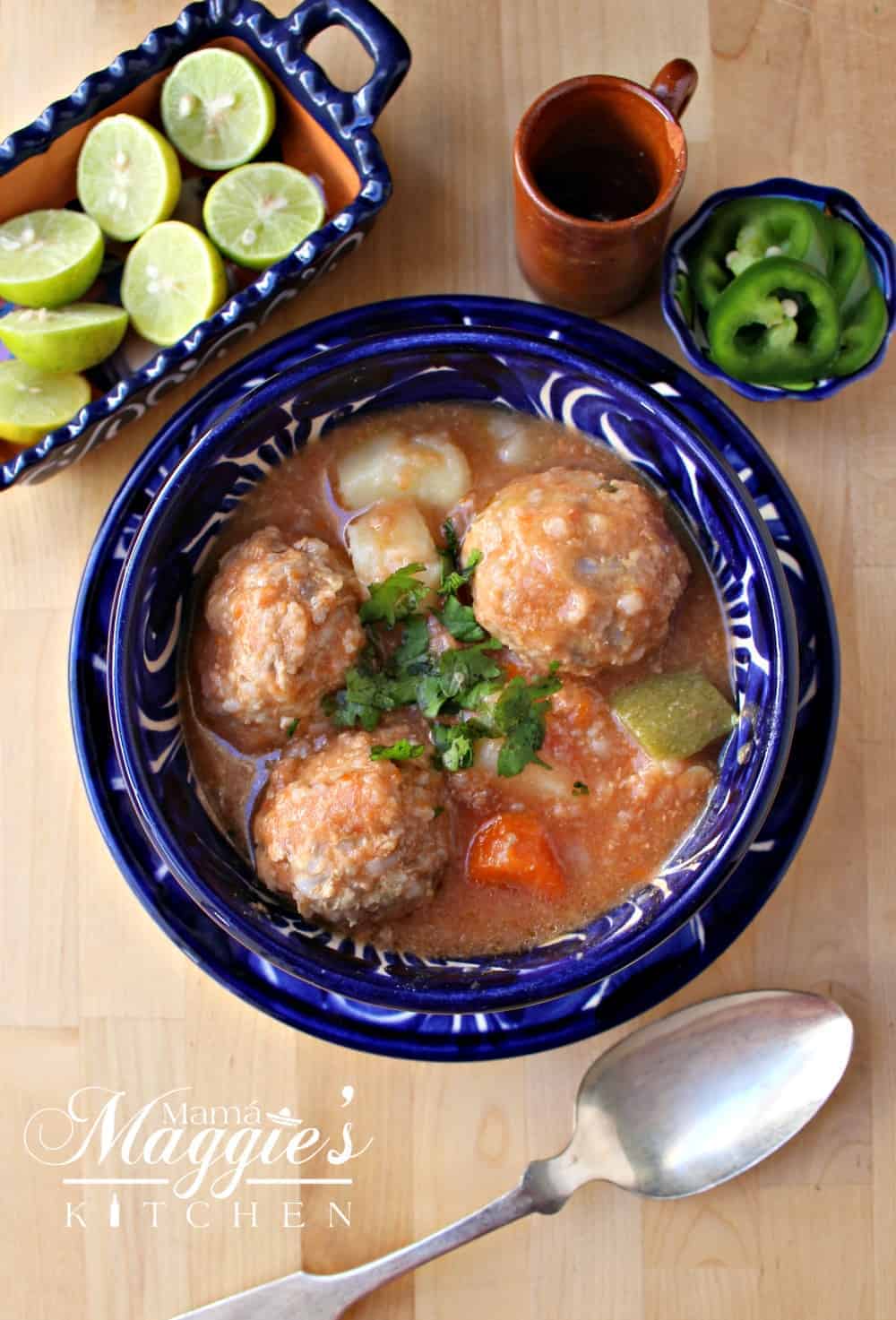 Albóndigas en Caldillo (or Mexican Meatball Soup) in a decorative blue bowl next to lime and a spoon.