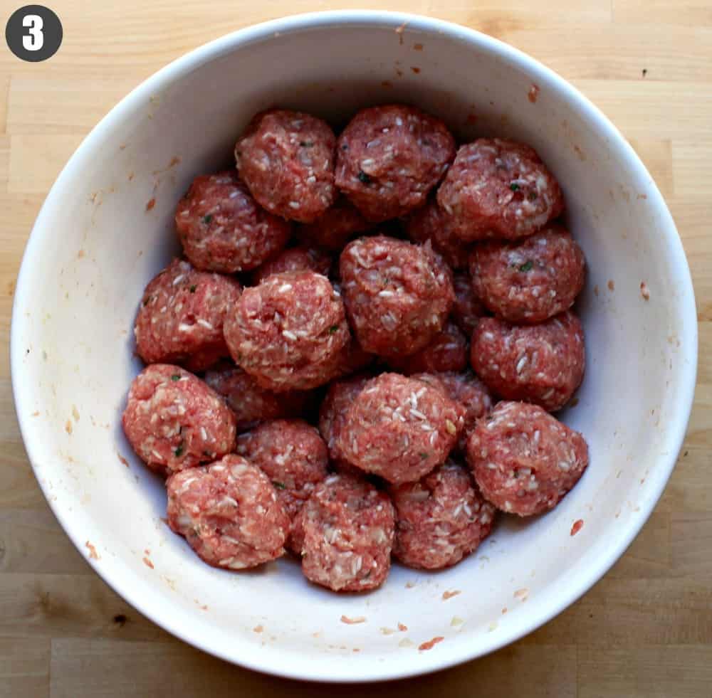 A large white bowl full of raw meatballs.