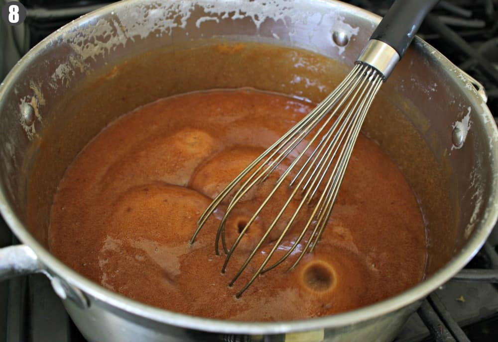 A bubbling cajeta inside a stock pot with a whisk. 