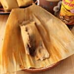 A Tamal de Mole unwrapped but lying on top of the corn husk and next to more tamales.