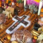A cross on a Day of the Dead altar surrounded by marigolds, candles, and bread.