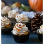 An image of a pumpkin cupcake with cajeta frosting surrounded by more cupcakes and a pinecone.