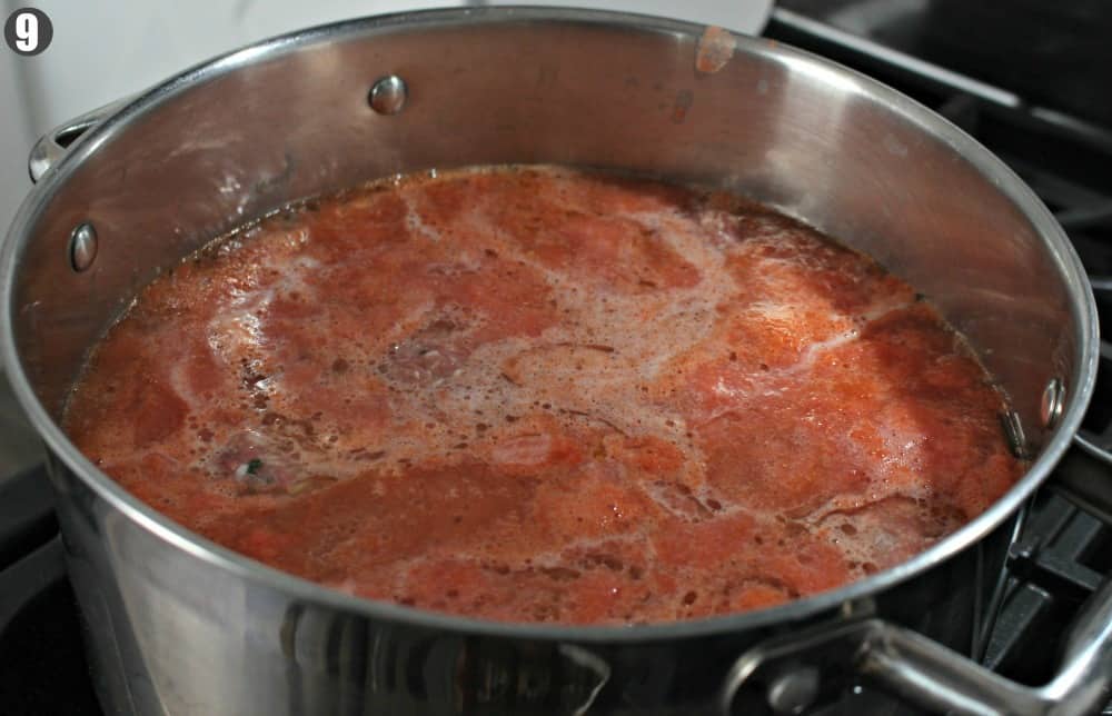 A large stock pot with tomato sauce and meatballs cooking on a stove. 