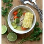 Mexican Chicken Soup in a white bowl surrounded by lime and cilantro leaves.
