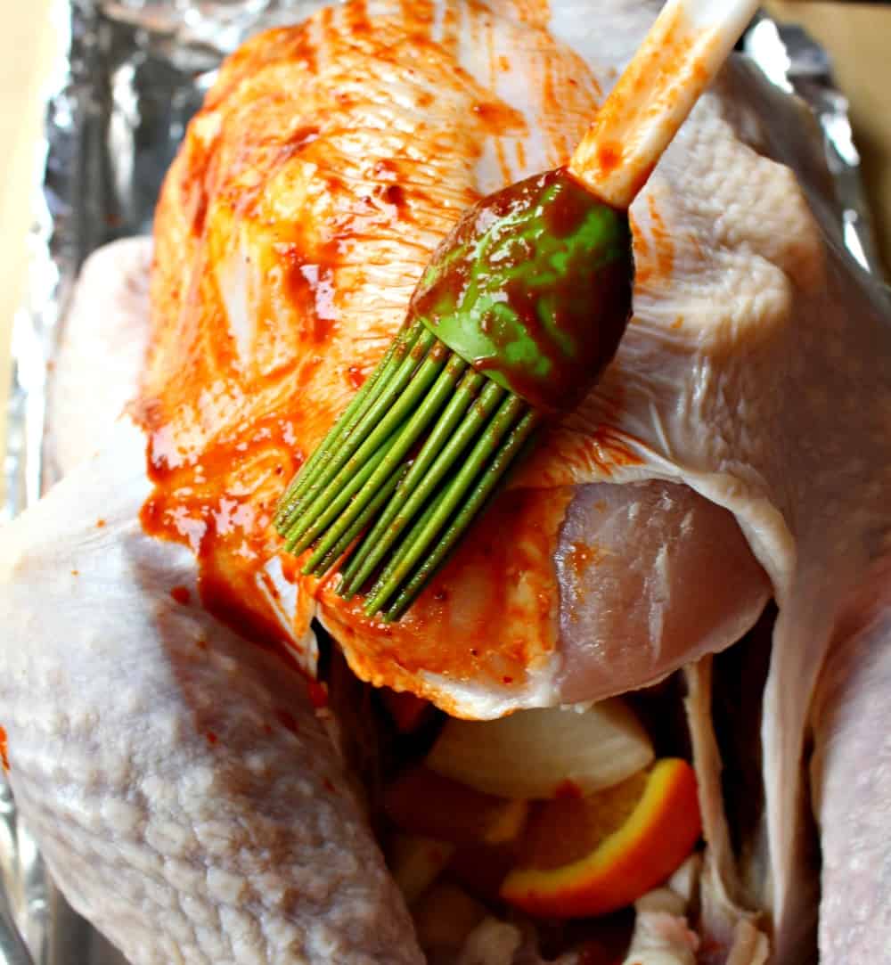 A cooking brush brushing the sauce on a raw turkey.