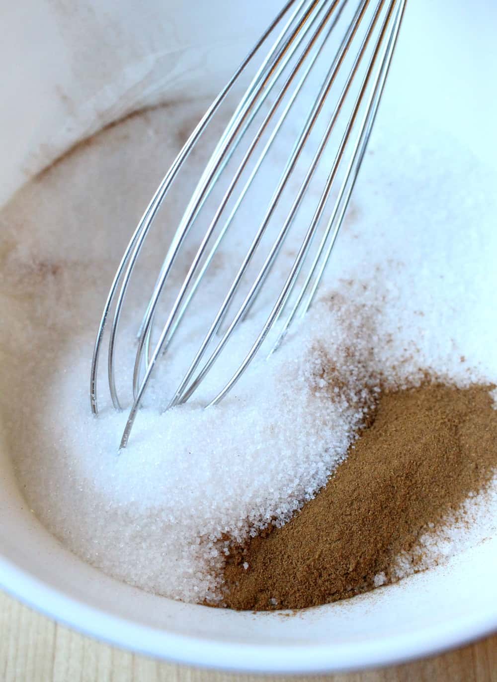 Cinnamon and sugar in a white bowl with a whisk.