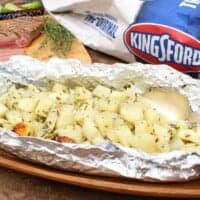 A picture of potatoes wrapped in a foil packet next to a package of Kingsford charcoal.
