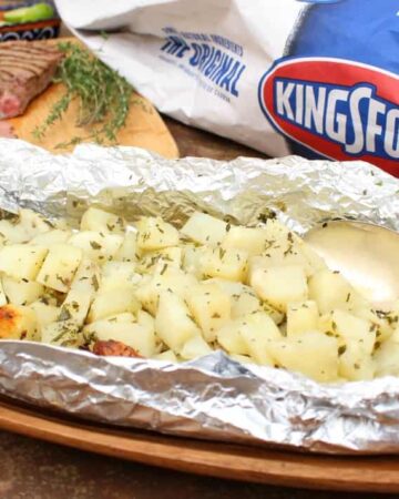 A picture of potatoes wrapped in a foil packet next to a package of Kingsford charcoal.