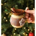Hand holding a decorative clay mug with Ponche Navideno next to a Christmas tree.