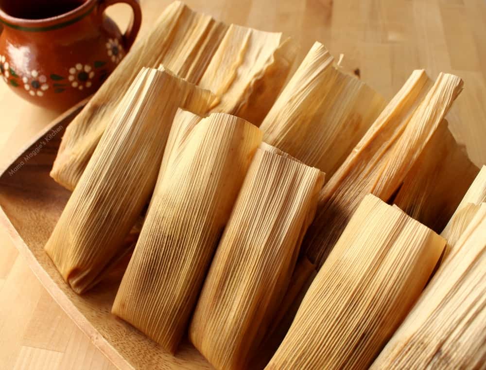 Tamales on a wooden platter next to a decorative clay mug. 