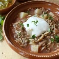 Fideo con Carne in a clay bowl topped with sour cream and chopped cilantro.