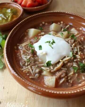 Fideo con Carne in a clay bowl topped with sour cream and chopped cilantro.