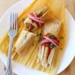 Two turkey pibil tamales on a corn husk topped with pickled red onions and chopped cilantro.