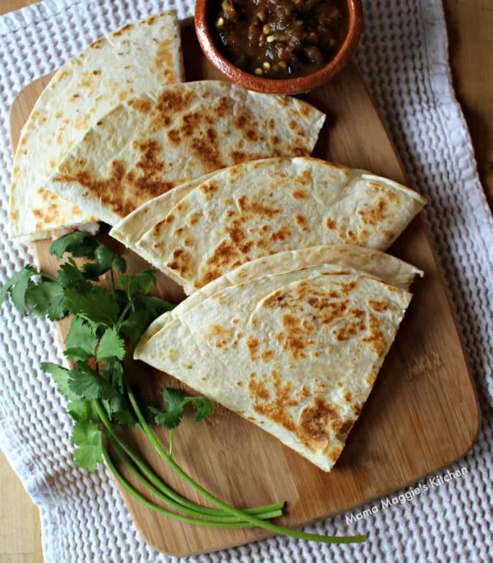 Shrimp Poblano Quesadillas on a wooden cutting board surrounded by cilantro leaves and salsa.