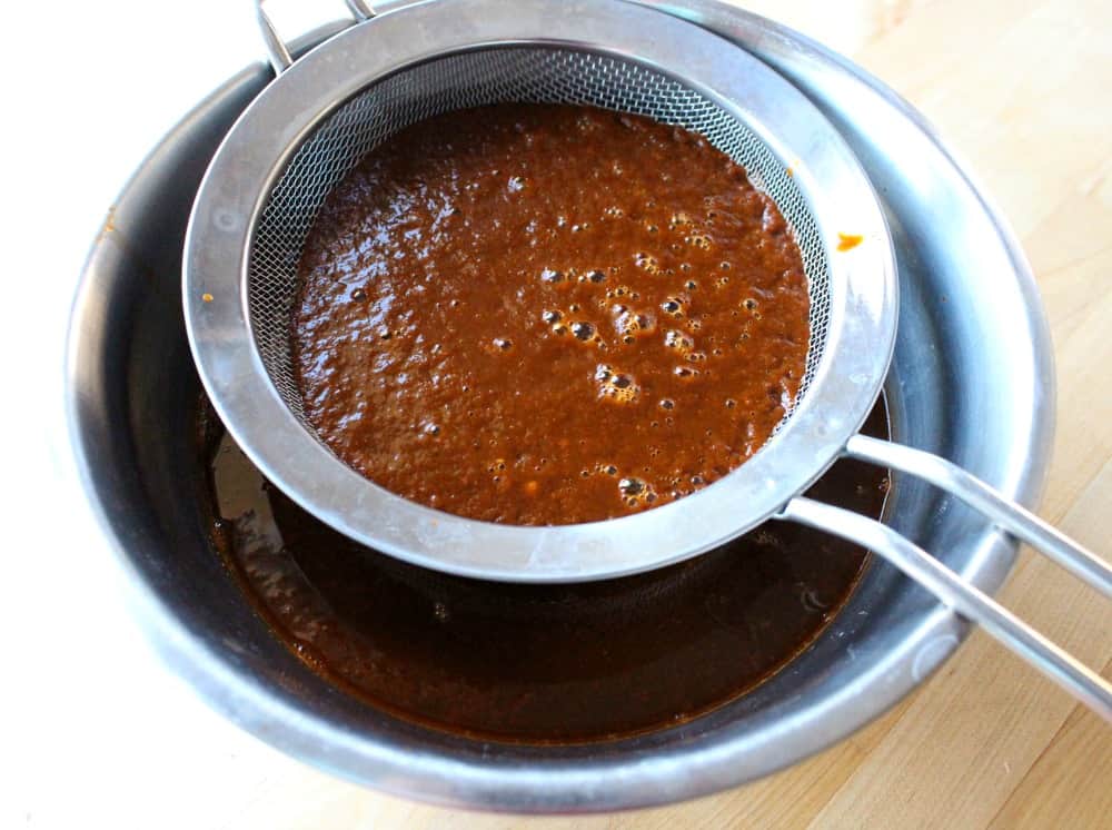 A colander above a metal bowl straining adobo sauce.