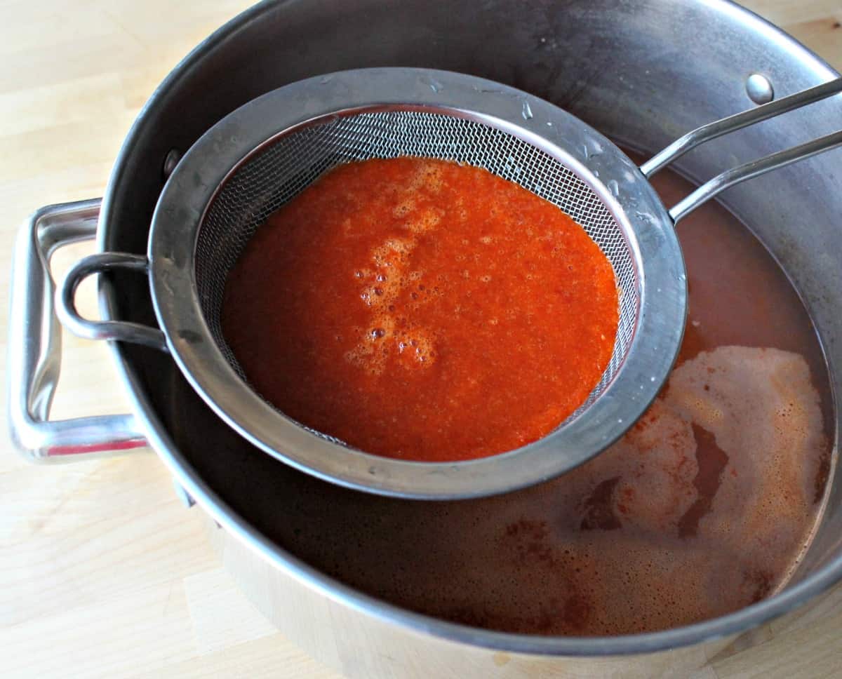 A strainer with red chile sauce over a stock pot.