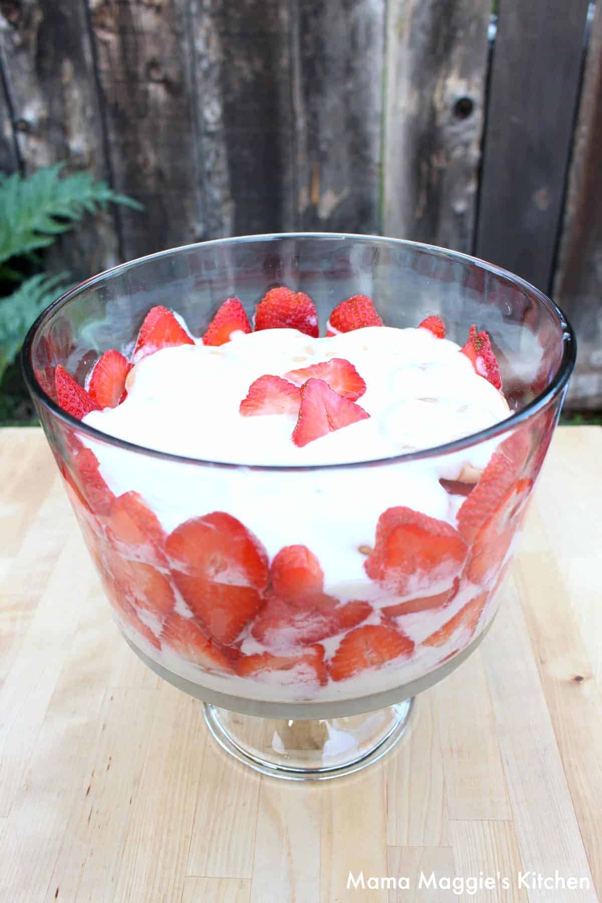 A Carlota de Fresa trifle with a wooden fence and green branch in the background.
