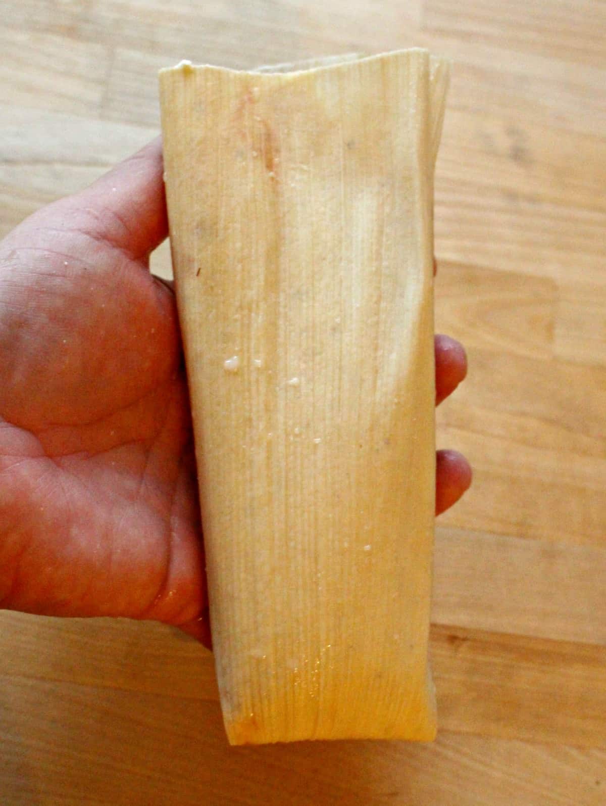 Hand holding an assembled but uncooked tamal.
